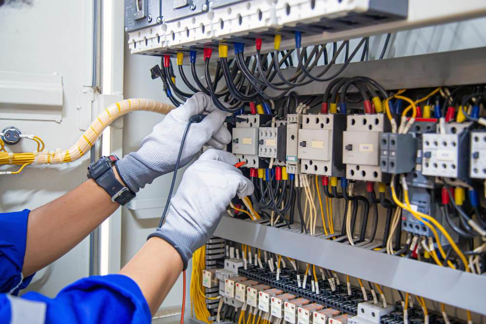 technicien de maintenance en électricité tenant à la main un voltmètre à courant alternatif vérifiant la tension du courant électrique au niveau des disjoncteurs